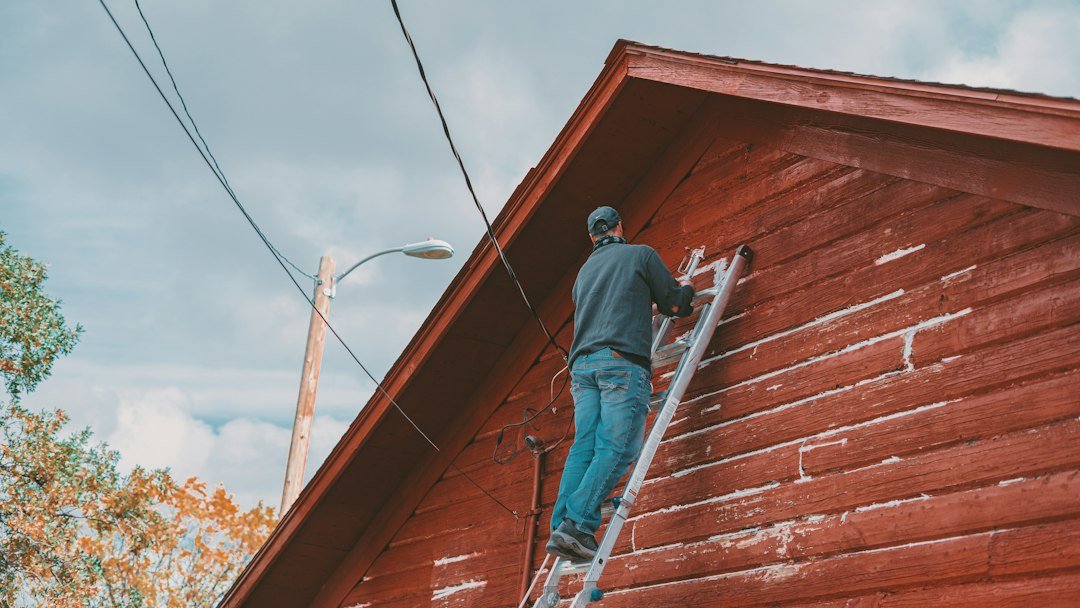 Worker standing on a ladder while painting the exterior wall of a building