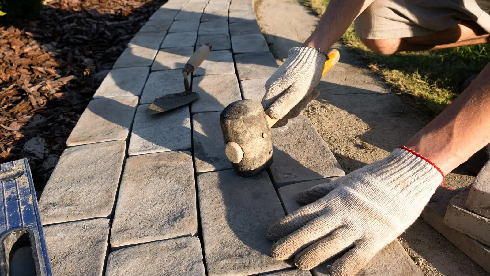 Gloved hands setting concrete pavers for a curved garden path with a rubber mallet